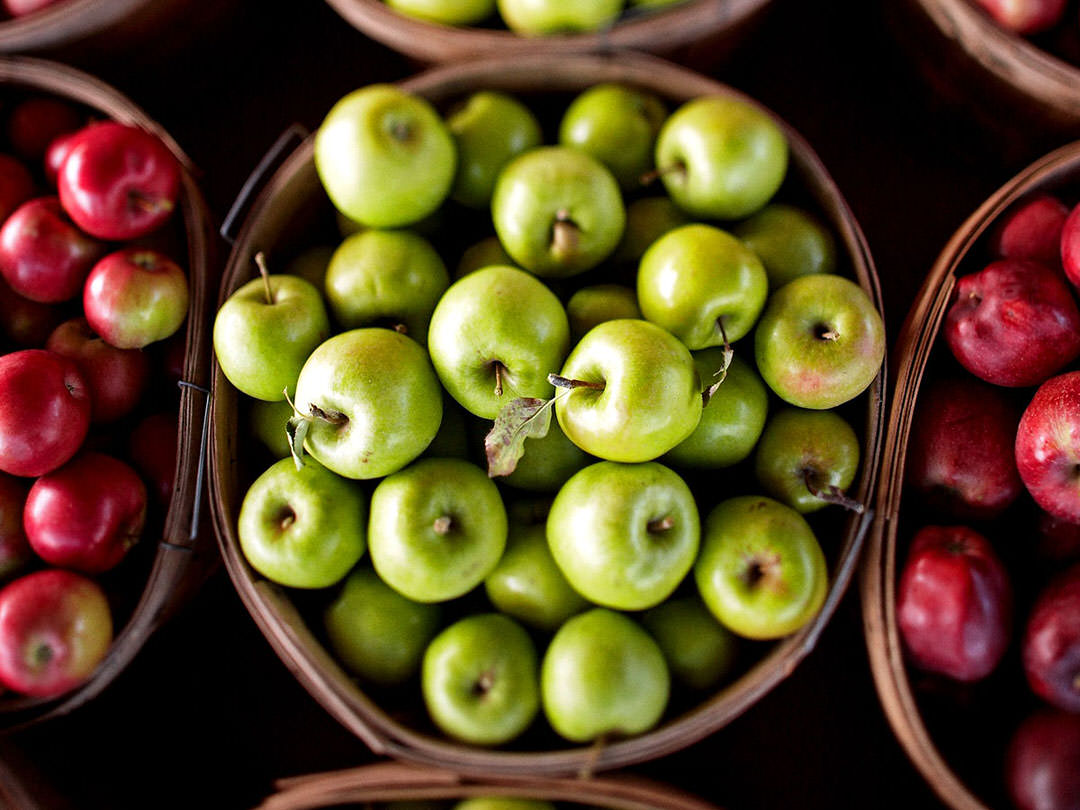 A bushel of granny smith apples rests on a market table amidst other varieties.