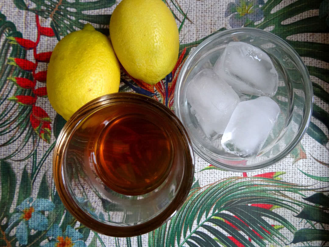 A glass of whisky and glass of ice sit beside two lemons on a table