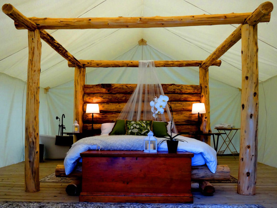 A timber-framed four-postered bed sits in the middle of a large white tent.