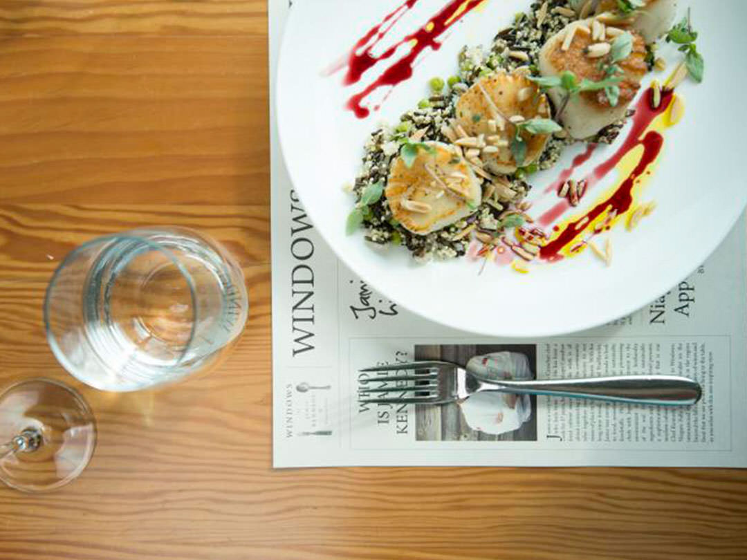 A plate of scallops awaits to be eaten beside a fork and a glass of water on a table.