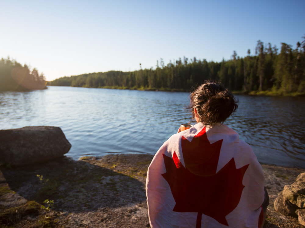 Una niña envuelta en una toalla con la bandera canadiense se sienta a admirar un hermoso lago