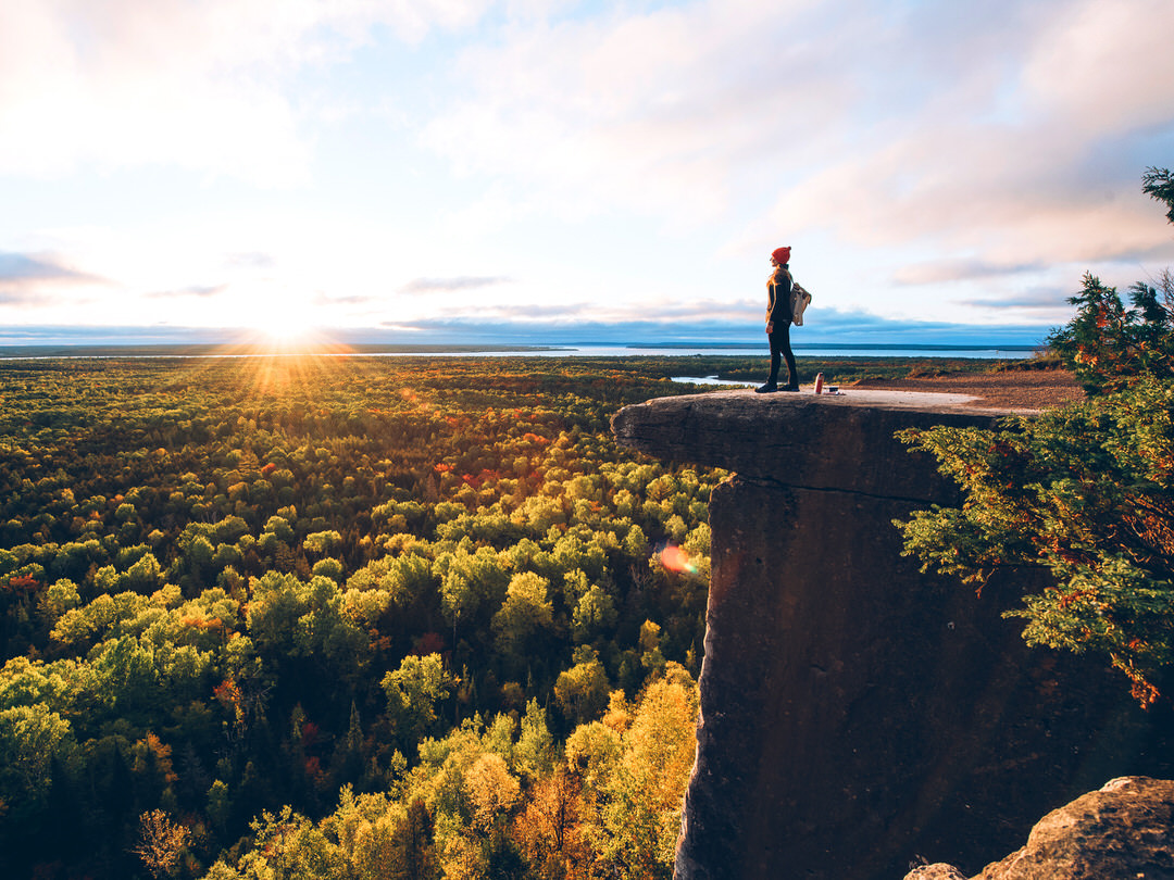Eine Frau steht auf einem Felsvorsprung mit Blick auf eine malerische Landschaft in Herbstfarben