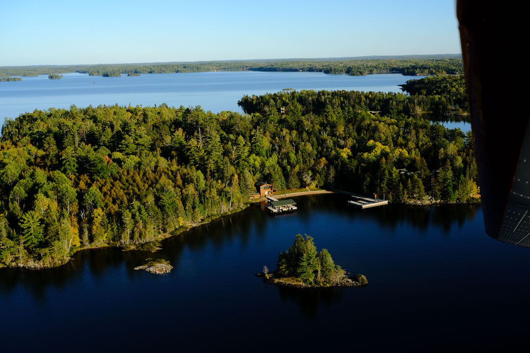 Blick von oben auf die dichte Wildnis, unberührtes Wasser und eine abgelegene Lodge am Lake of the Woods