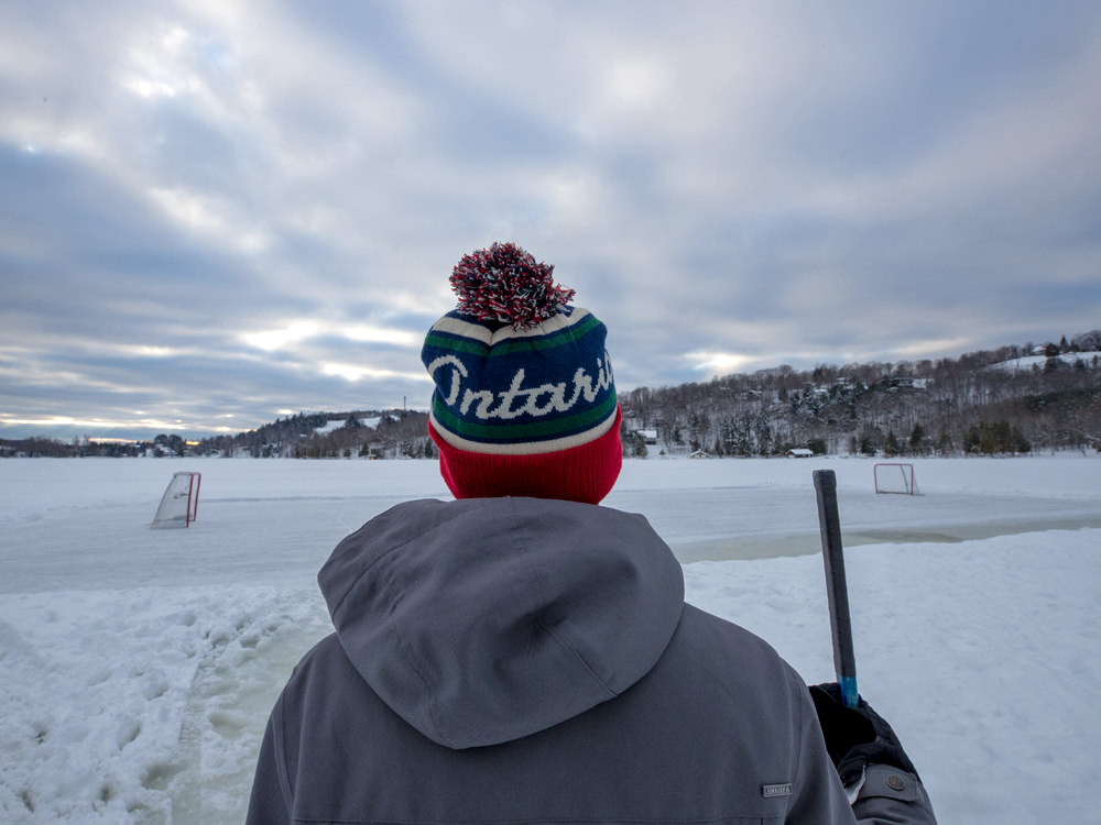 Ein junger Mann steht vor einer Teich-Eishockeybahn und hält einen Hockeyschläger
