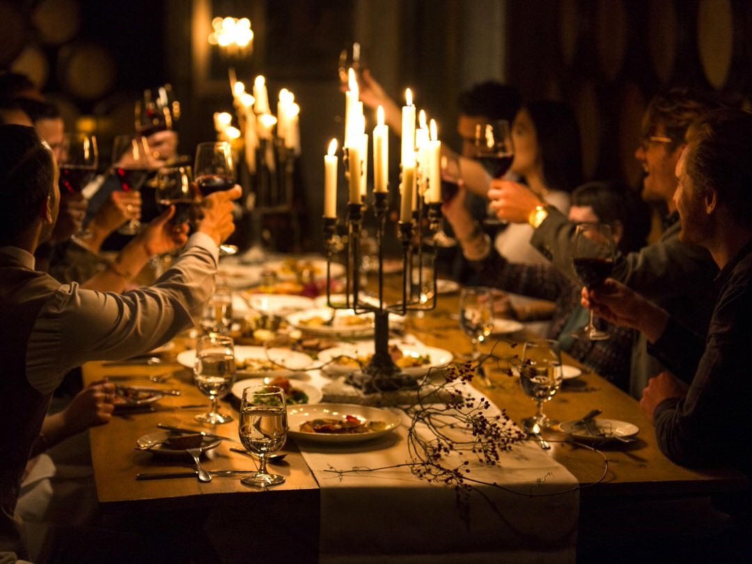 Un groupe d'amis trinque avec du vin à une table aux chandelles