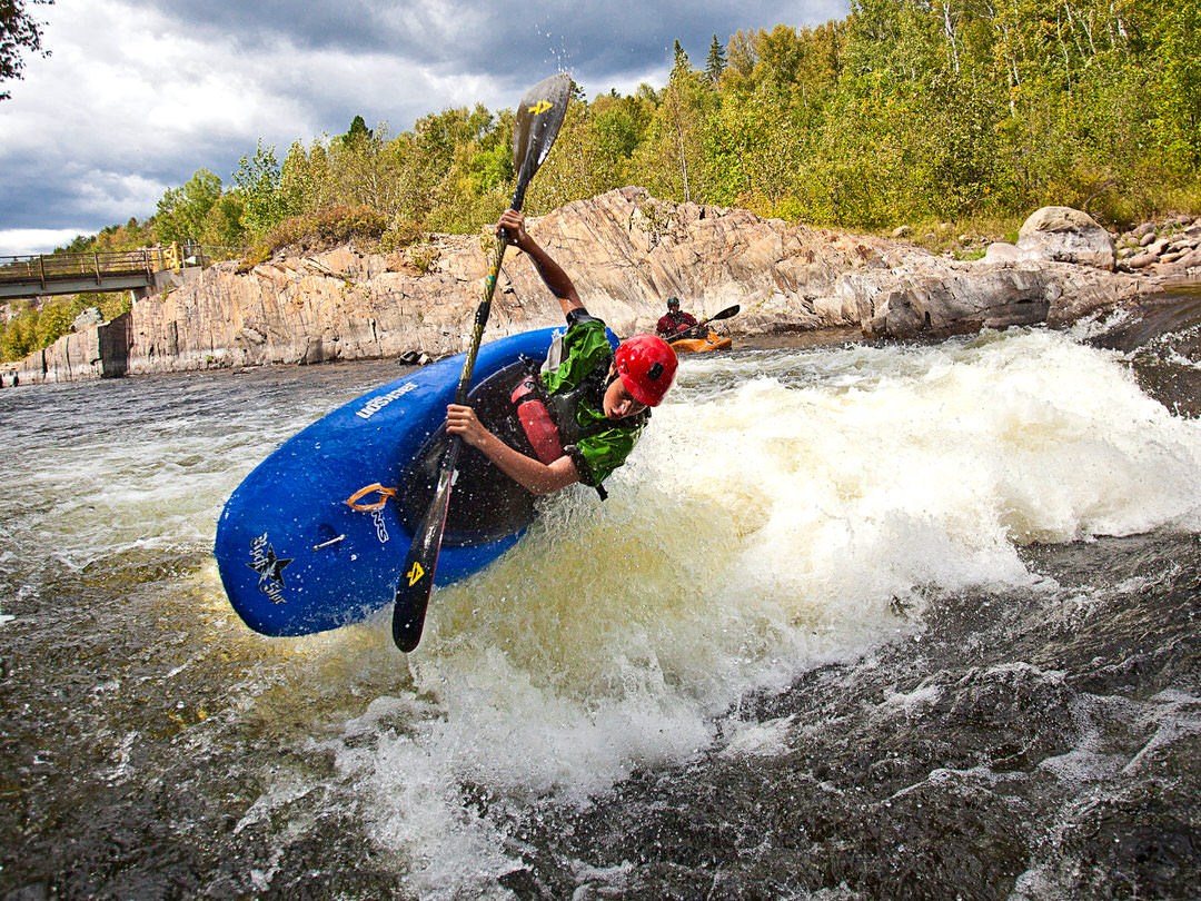 A man in a blue sport kayak rides a rough wave