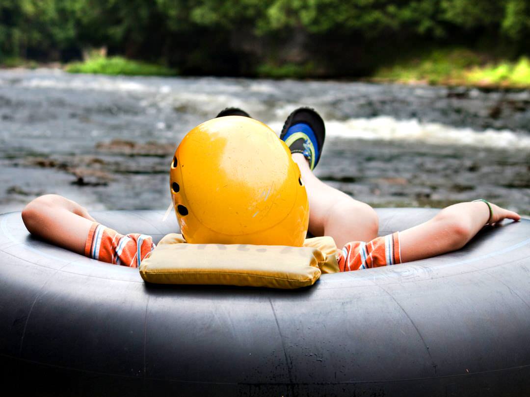 Ein kleiner Junge schwimmt in einem Schlauch einen Fluss hinunter