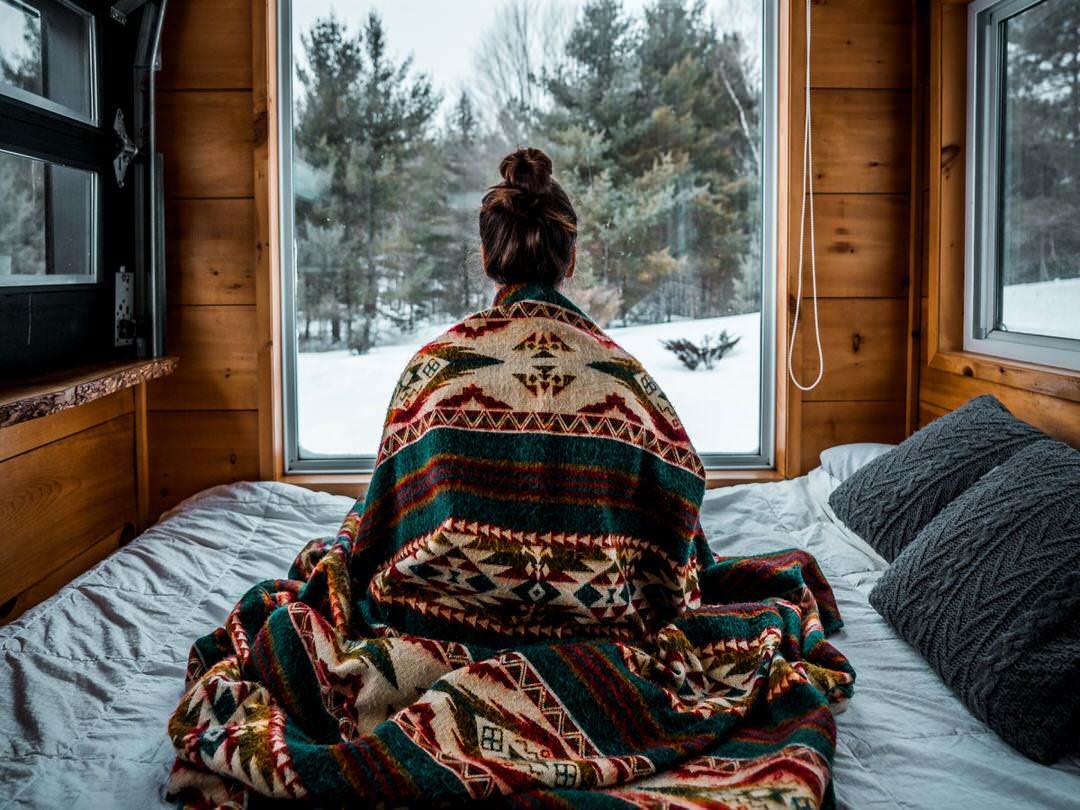 Young girl draped in a blanket and looking out the window