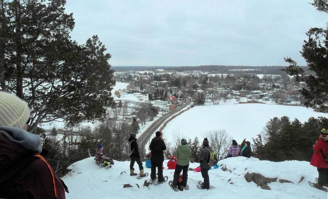 Un groupe de personnes en raquettes au sommet d’une colline regardant la petite ville qui se trouve plus bas.
