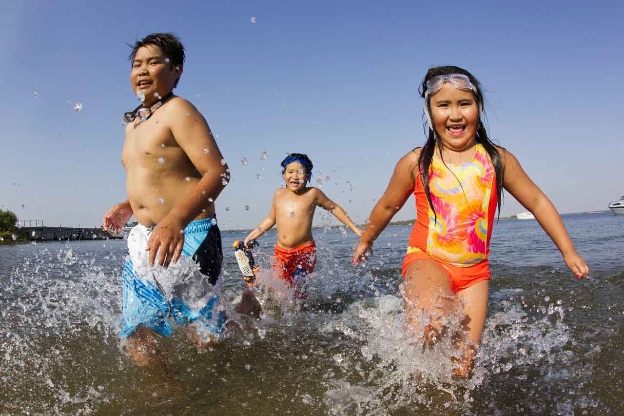 A girl and a boy running in the water with a boy chasing them to the shore