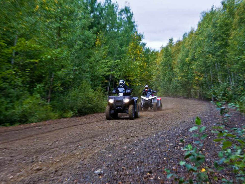Zwei Leute, die ATVs entlang einer Schotterstraße fahren