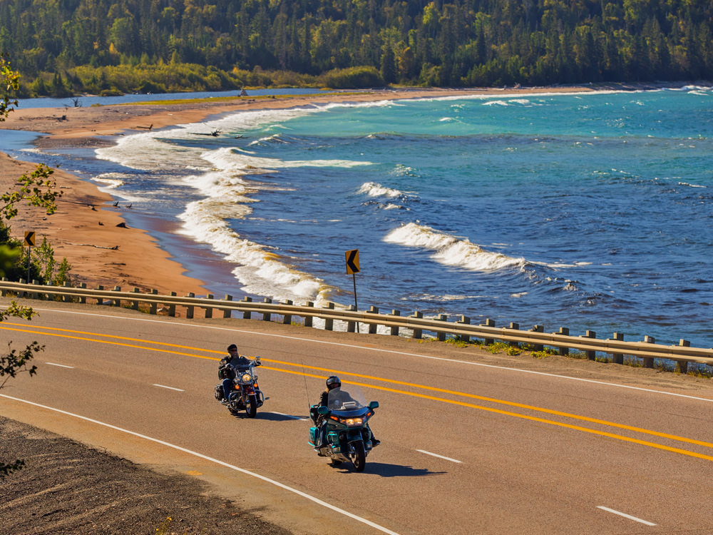 Dos motociclistas pasan frente a una playa de arena