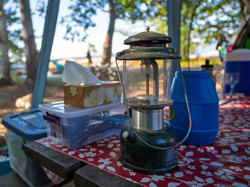 Geschirr, eine Laterne und andere Campingutensilien stehen auf einem Picknicktisch