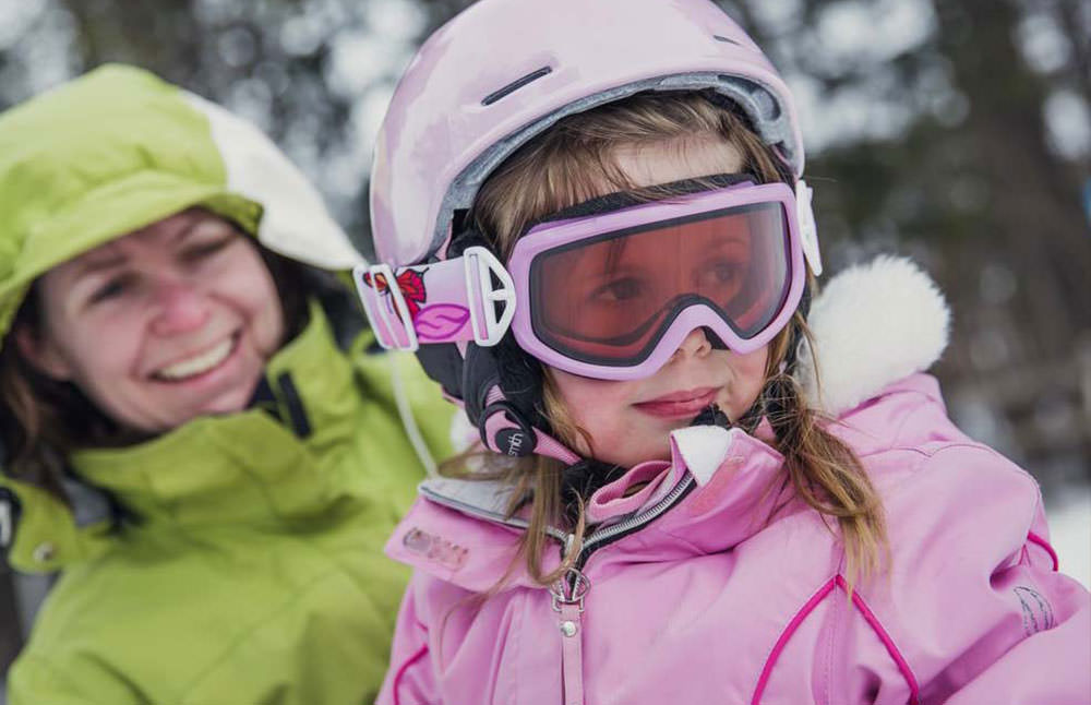 A mother and daughter smile, while looking at the snow outside