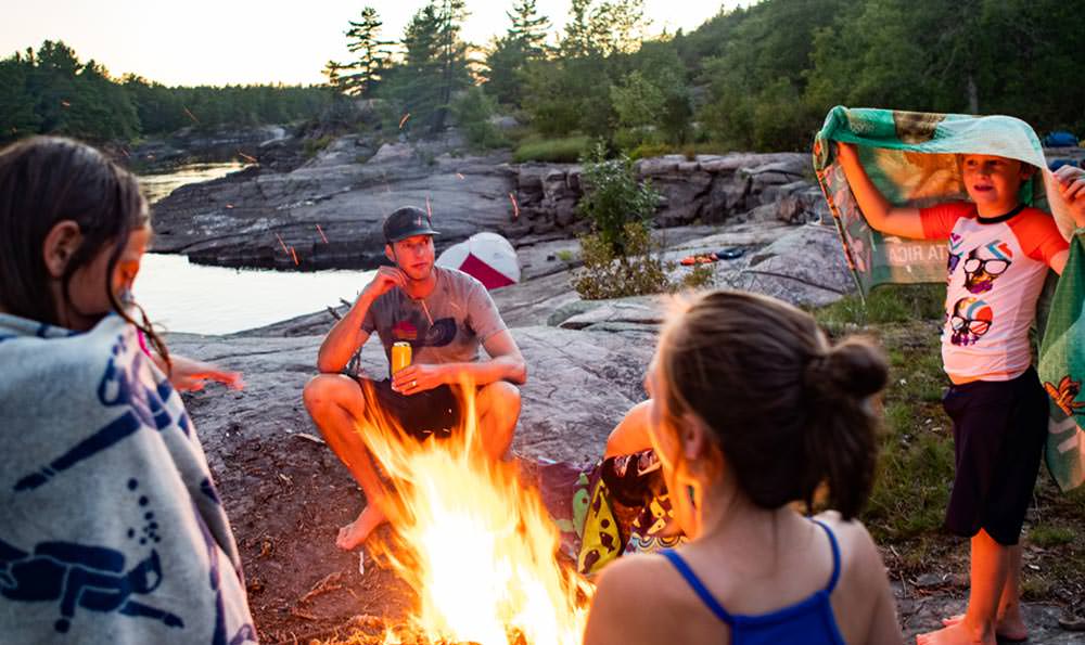 Eine Familie versammelt sich um ein Lagerfeuer an einem Fluss