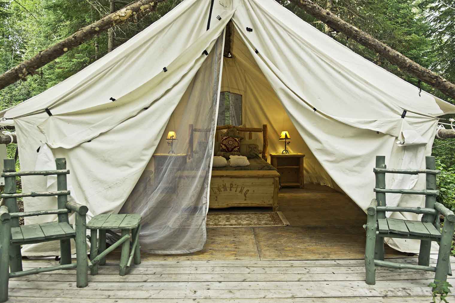 Una cama con armazón de madera se encuentra en medio de una gran carpa blanca.