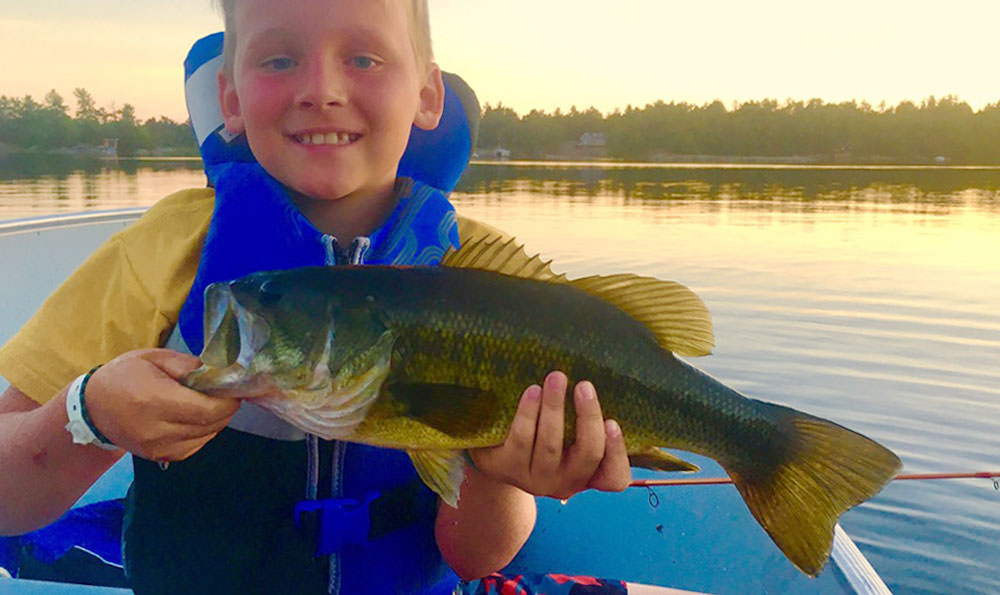Ein kleiner Junge in einem Boot hält stolz einen Fisch hoch, den er bei einem Angelausflug mit der Familie gefangen hat