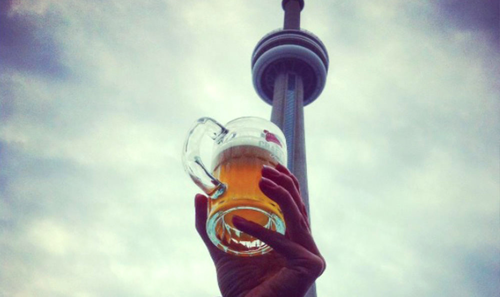 Eine Hand, die einen Bierkrug mit dem CN Tower im Hintergrund hält.
