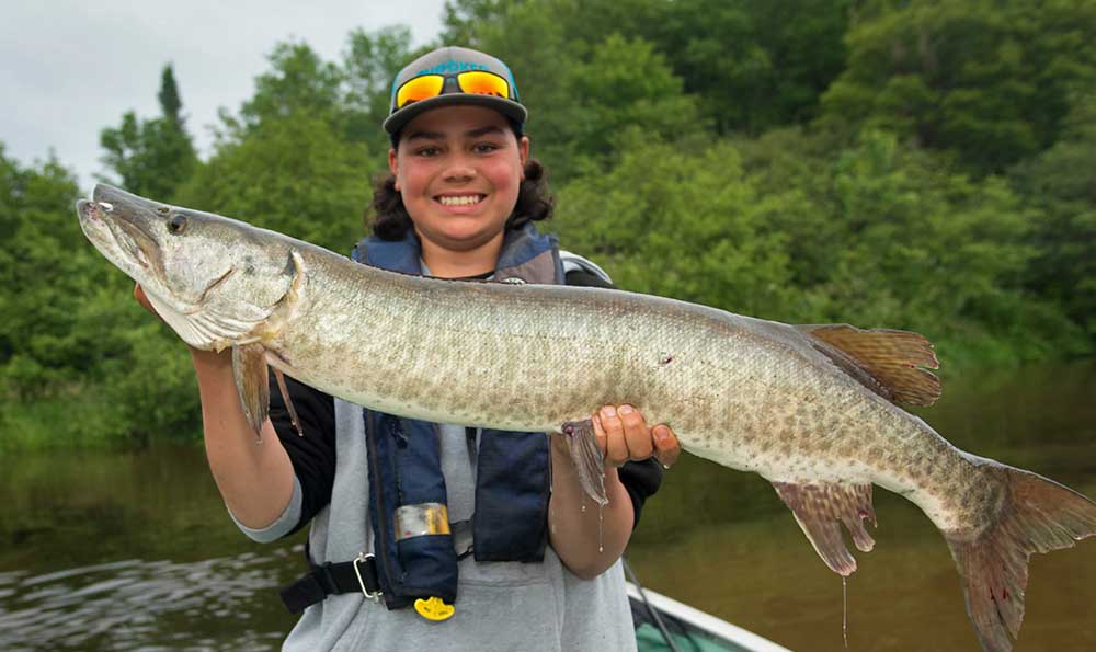 Ein junger Mann in einem Boot hält einen Muskie, der in einer hinteren Bucht des Nordkanals des Lake Huron gefangen wurde