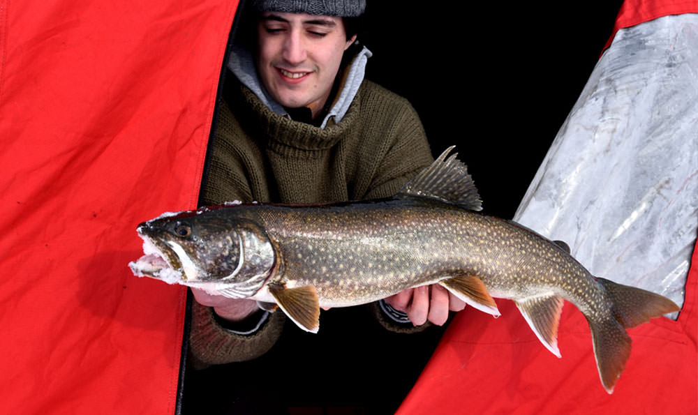 Un joven sostiene un pez dentro de una carpa de pesca en hielo