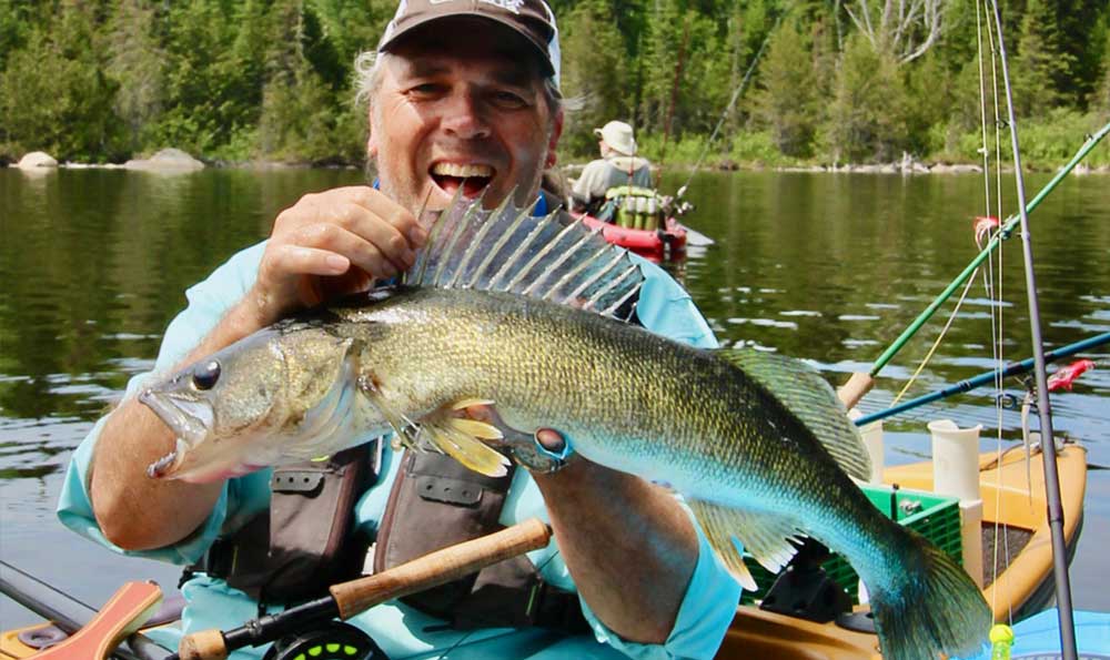 Ein Fliegenfischer, der von einem Kajak aus fischt, hält einen Zanderfang hoch