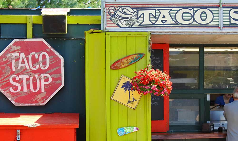 A person orders from the window of taco food truck stand