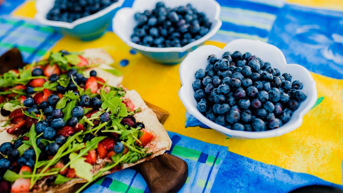 tres tazones de arándanos y pizzas cubiertas con arándanos se sientan en una mesa