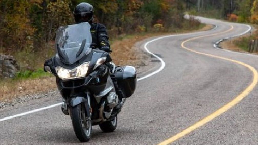 Un motociclista recorre un camino sinuoso que pasa por un bosque iluminado con colores otoñales