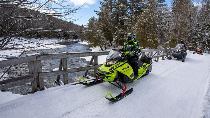 雪に覆われた橋で川を渡るスノーモービルのグループ。