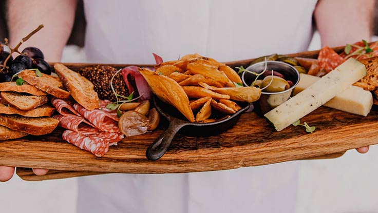Un chef presenta una tabla de charcutería con carnes y quesos.