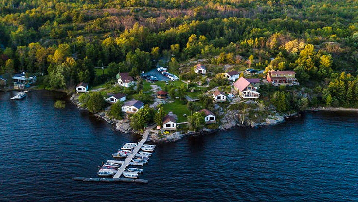 Vista de un resort de pesca y cabañas a la orilla de un lago rodeado de bosque.