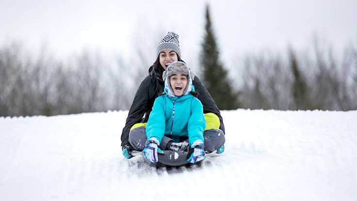 Dos personas sonrientes cabalgando por una colina cubierta de nieve en un tobogán.
