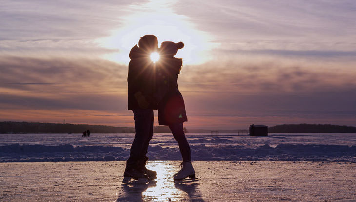 A couple taking a moment to kiss on a skating rink.