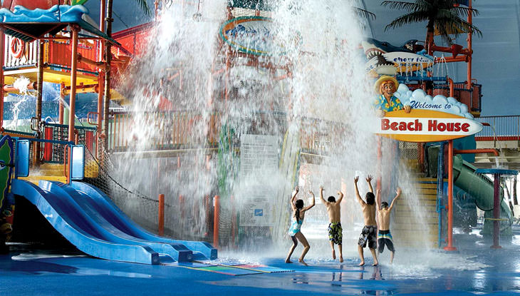 Cuatro niños juegan bajo una cascada en un parque acuático cubierto.