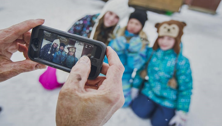A woman takes a photo of three children on the ice in front of an ice fishing hut.