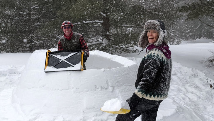 A man and woman having fun building a snow fort together.