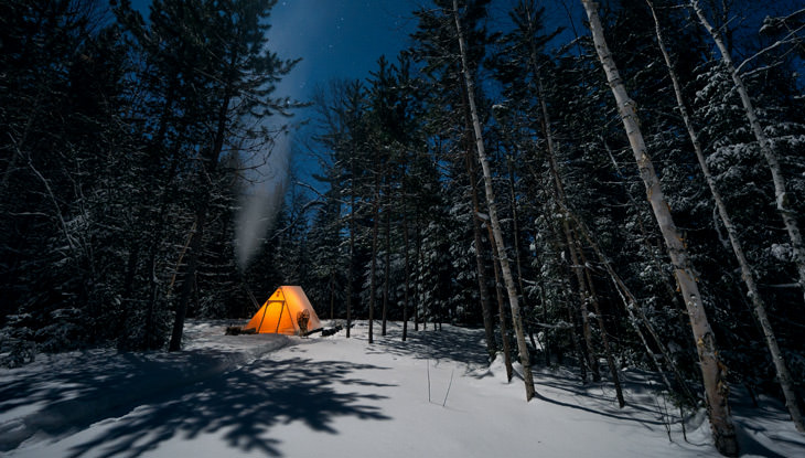 Una carpa se ilumina en la oscuridad en un campamento de invierno en el bosque.