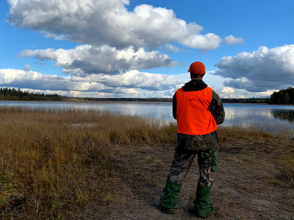 Un homme portant un gilet orange chasseur et une casquette regarde vers un lac