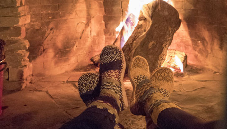 Two pairs of feet in warm slippers cozy in front of a fireplace.